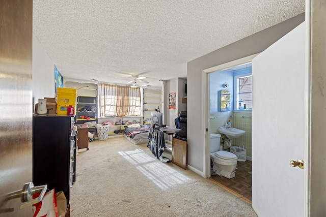 interior space with a textured ceiling, ensuite bathroom, ceiling fan, and tile walls