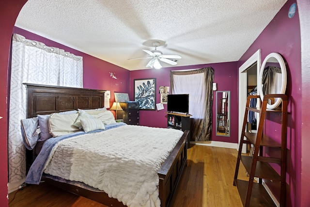 bedroom with a textured ceiling, ceiling fan, and dark hardwood / wood-style floors