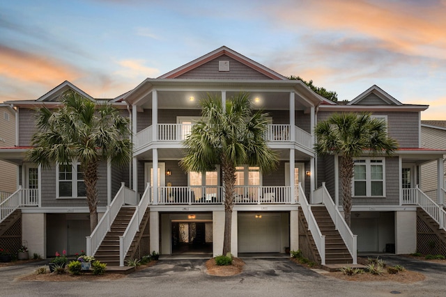 coastal home with aphalt driveway, a balcony, covered porch, stairs, and an attached garage