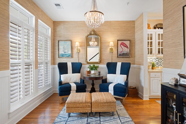 living area featuring an inviting chandelier, light wood-style flooring, a wainscoted wall, and visible vents
