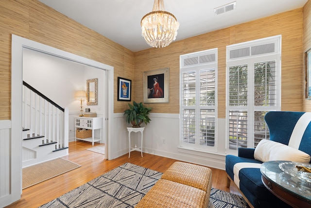 living area featuring a chandelier, a wainscoted wall, stairs, wood finished floors, and visible vents