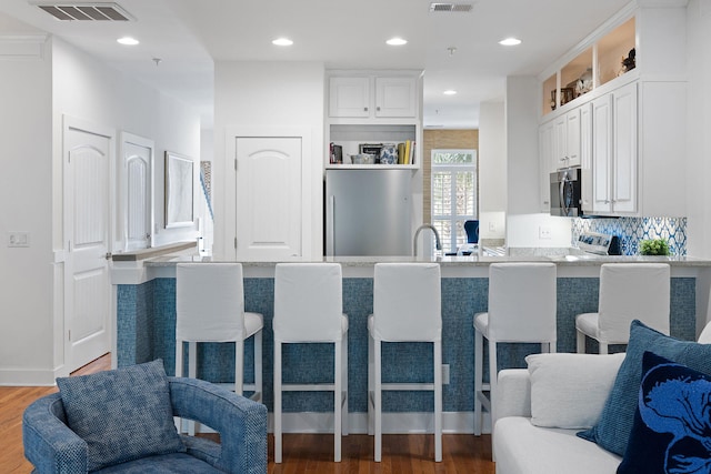 kitchen featuring white cabinets, stainless steel appliances, visible vents, and a breakfast bar