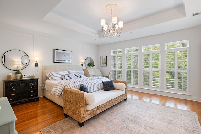 bedroom featuring a notable chandelier, wood finished floors, a tray ceiling, and multiple windows