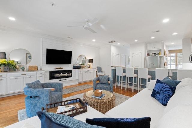 living area featuring crown molding, a ceiling fan, light wood-type flooring, and visible vents
