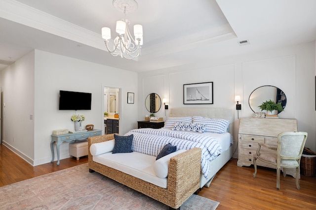 bedroom featuring an inviting chandelier, visible vents, wood finished floors, baseboards, and a tray ceiling