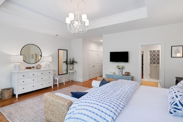 bedroom featuring an inviting chandelier, baseboards, a tray ceiling, and wood finished floors