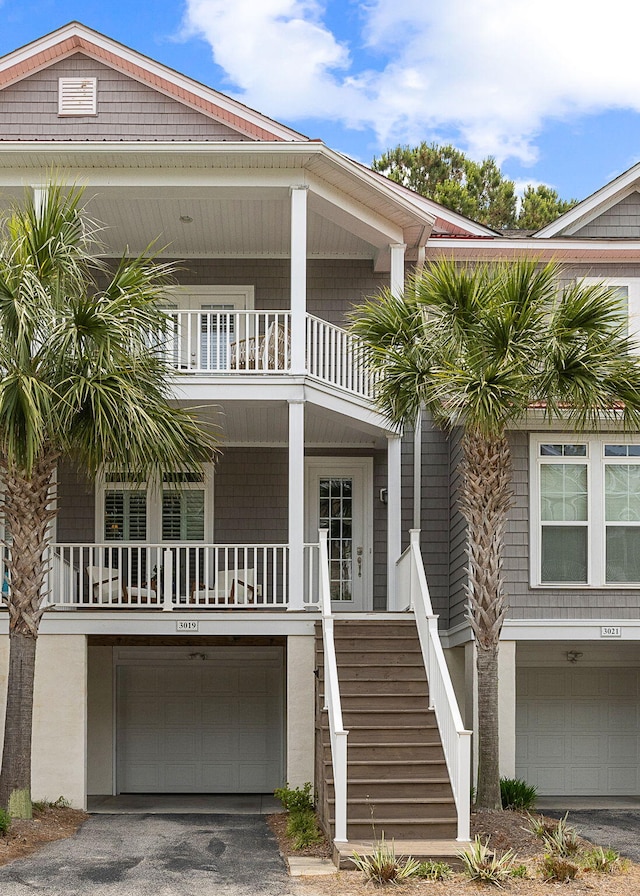 coastal inspired home with an attached garage, a balcony, stairs, and aphalt driveway