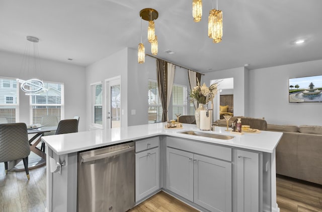 kitchen with light hardwood / wood-style flooring, stainless steel dishwasher, a notable chandelier, pendant lighting, and a kitchen island with sink