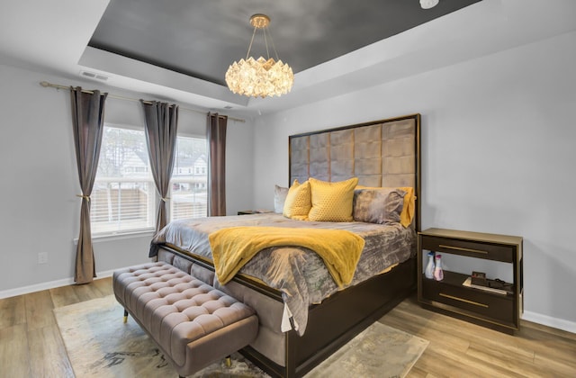 bedroom with light hardwood / wood-style flooring, a raised ceiling, and a chandelier