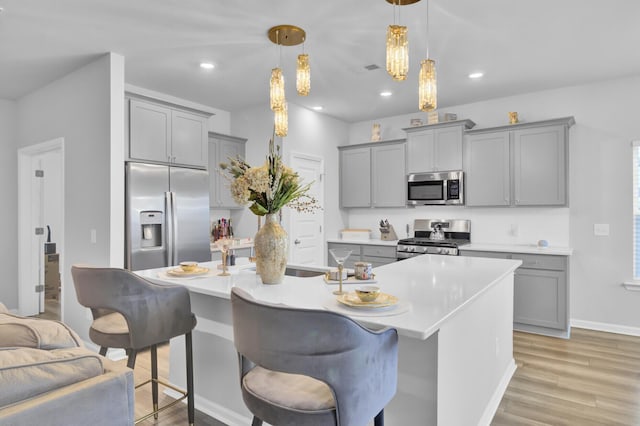 kitchen with hanging light fixtures, appliances with stainless steel finishes, gray cabinets, and a center island with sink