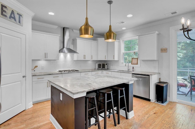 kitchen with a center island, sink, wall chimney exhaust hood, appliances with stainless steel finishes, and white cabinetry