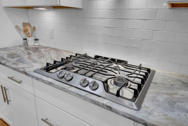 room details with light stone counters, white cabinetry, backsplash, and stainless steel gas cooktop