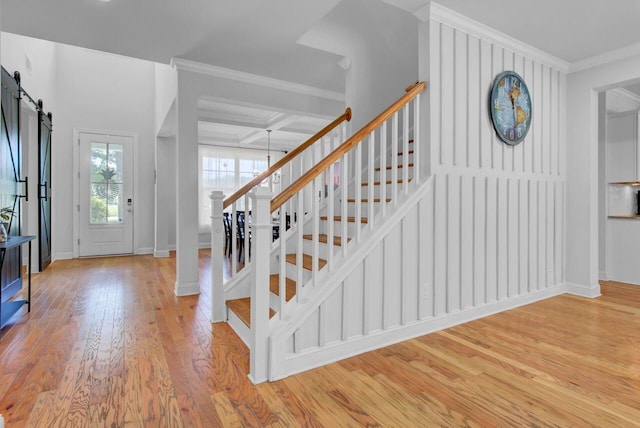 foyer featuring coffered ceiling, a barn door, light wood-type flooring, ornamental molding, and beam ceiling