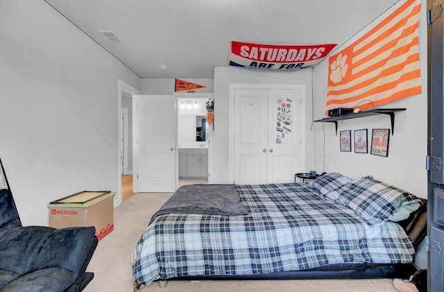 bedroom with ensuite bathroom and light carpet