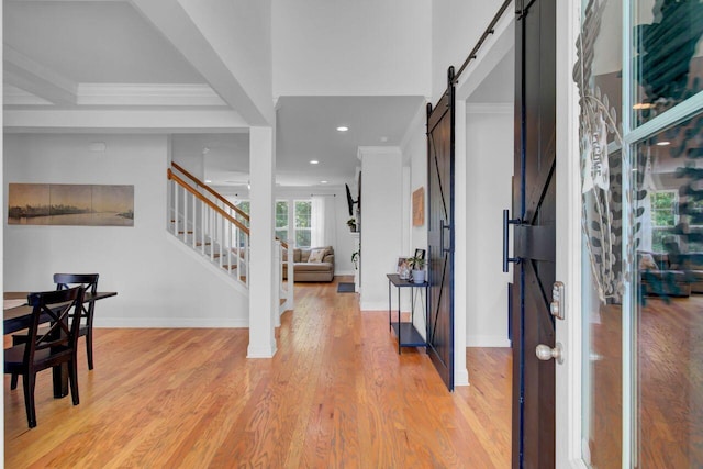 foyer entrance with a barn door, light hardwood / wood-style flooring, and ornamental molding