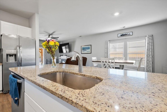 kitchen with appliances with stainless steel finishes, light stone countertops, ceiling fan, white cabinets, and sink