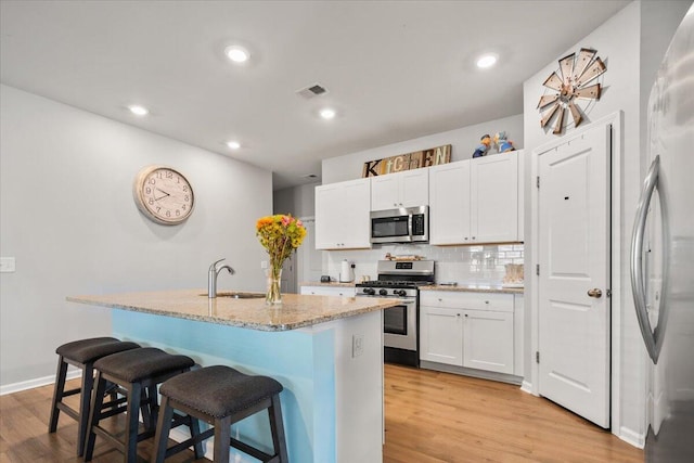 kitchen with stainless steel appliances, a kitchen island with sink, white cabinetry, a breakfast bar area, and sink