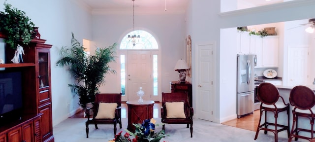 living area featuring a towering ceiling, ornamental molding, ceiling fan with notable chandelier, and light hardwood / wood-style floors