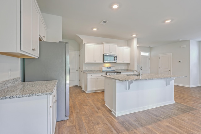 kitchen featuring stainless steel appliances, light wood-style floors, white cabinets, a breakfast bar area, and a sink