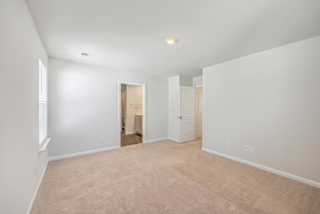 unfurnished bedroom with light colored carpet, baseboards, multiple windows, and ensuite bath