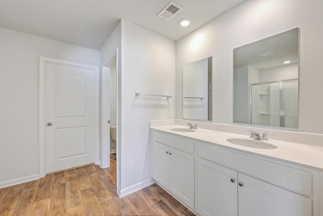 full bath featuring double vanity, toilet, wood finished floors, a shower with door, and baseboards