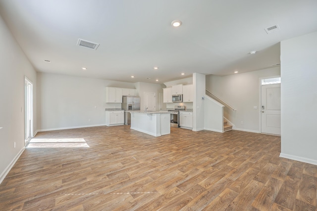 unfurnished living room featuring light wood-style flooring, stairs, baseboards, and recessed lighting