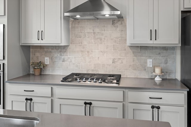 kitchen with decorative backsplash, stainless steel gas cooktop, white cabinets, and range hood