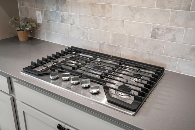 room details featuring decorative backsplash, white cabinets, and stainless steel gas stovetop