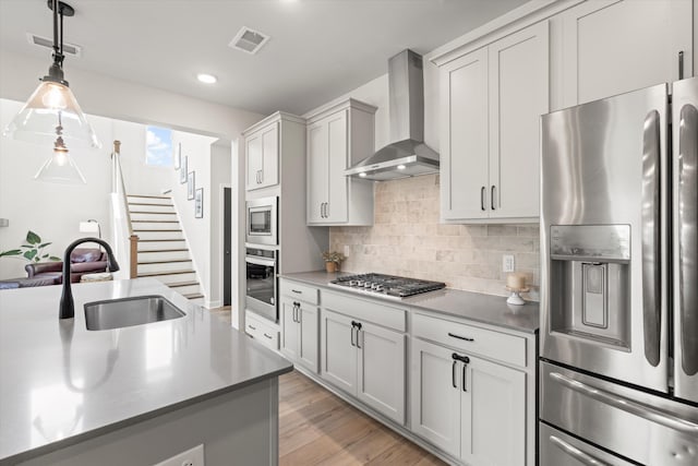 kitchen featuring appliances with stainless steel finishes, a sink, wall chimney exhaust hood, backsplash, and visible vents
