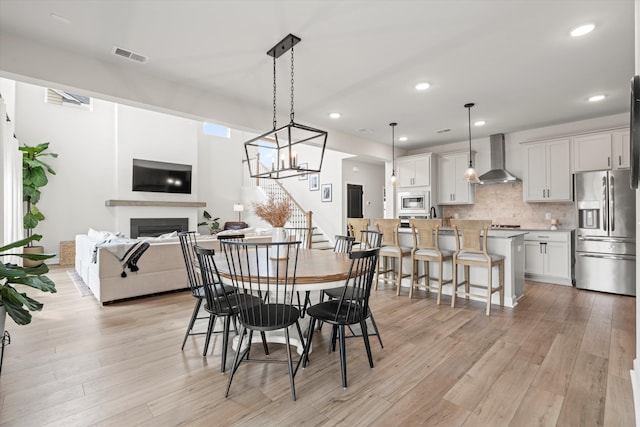 dining area with visible vents, light wood finished floors, stairs, and a fireplace