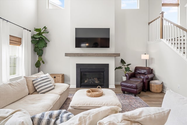 living room with a glass covered fireplace, stairs, wood finished floors, and a towering ceiling