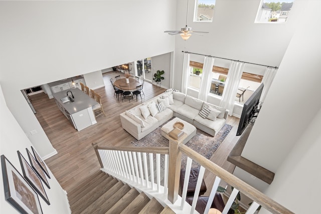 living room featuring wood finished floors, baseboards, ceiling fan with notable chandelier, and a high ceiling