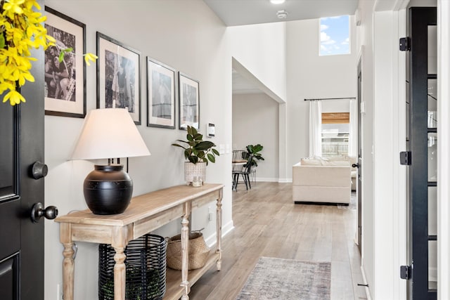hallway with arched walkways, baseboards, and light wood-type flooring