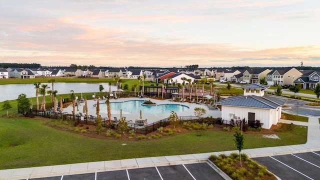 pool at dusk with a community pool, a lawn, a residential view, fence, and a water view