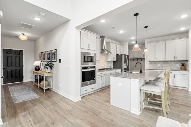 kitchen with wall chimney range hood, a sink, stainless steel appliances, tasteful backsplash, and visible vents