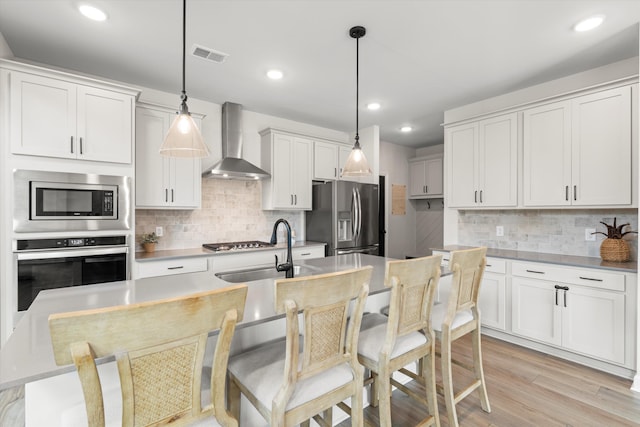 kitchen featuring wall chimney range hood, appliances with stainless steel finishes, decorative backsplash, and visible vents