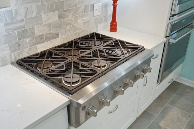 interior details featuring tasteful backsplash, dark tile patterned flooring, stainless steel appliances, light stone countertops, and white cabinetry