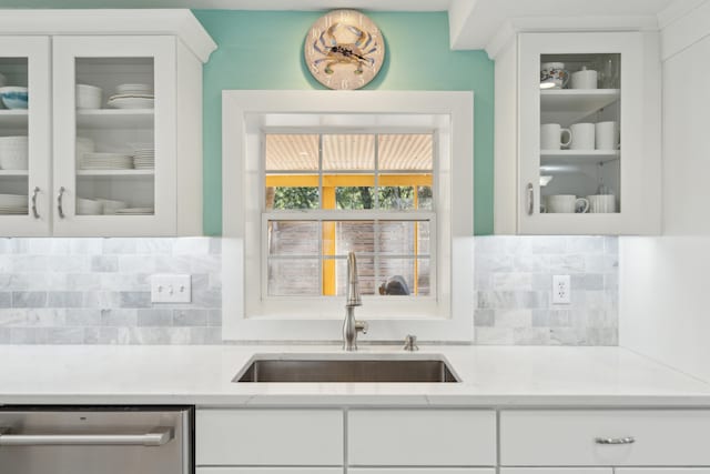 kitchen featuring tasteful backsplash, sink, light stone countertops, stainless steel dishwasher, and white cabinetry