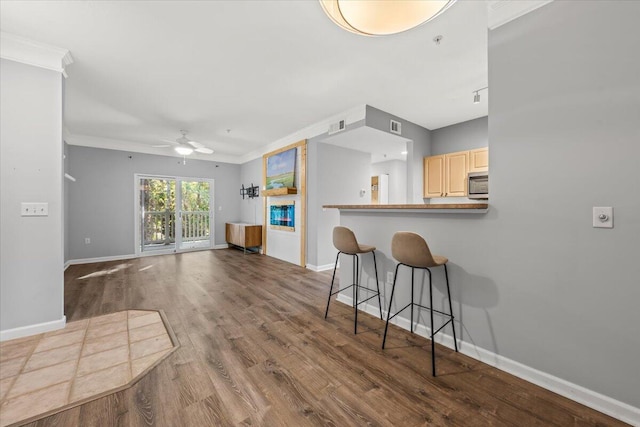 kitchen with hardwood / wood-style floors, cream cabinets, crown molding, ceiling fan, and a kitchen bar