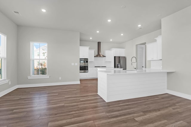 kitchen featuring white cabinets, wall chimney range hood, appliances with stainless steel finishes, dark hardwood / wood-style flooring, and kitchen peninsula