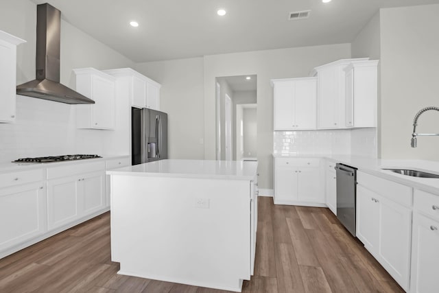 kitchen featuring appliances with stainless steel finishes, light wood-type flooring, wall chimney exhaust hood, sink, and a center island