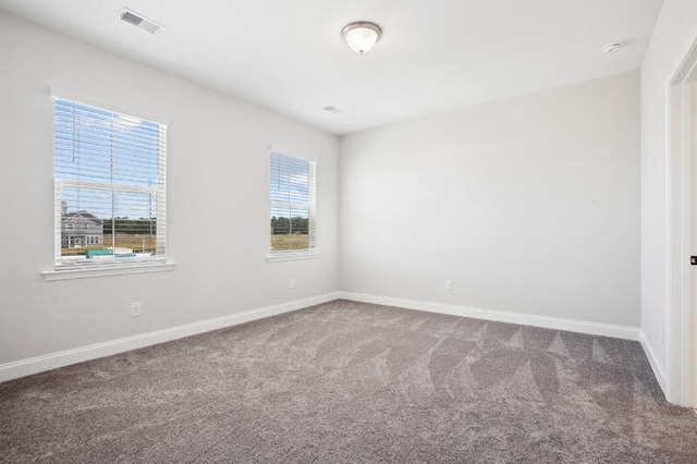 carpeted spare room with a wealth of natural light, visible vents, and baseboards