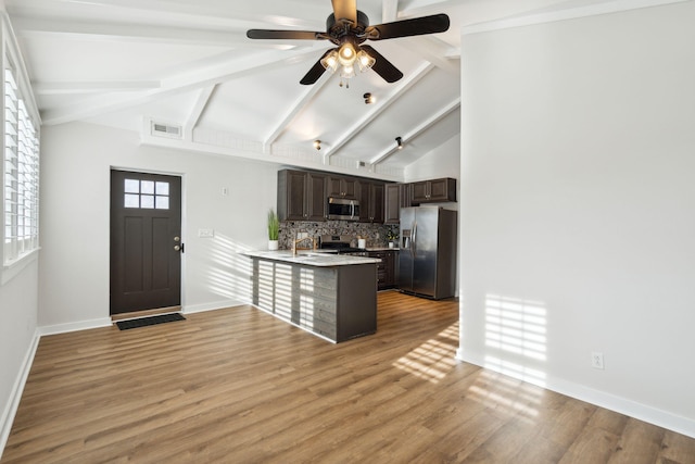 kitchen with lofted ceiling with beams, kitchen peninsula, decorative backsplash, dark brown cabinetry, and stainless steel appliances