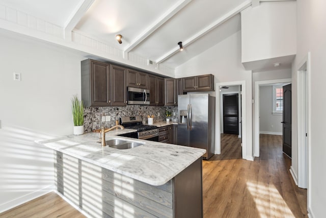 kitchen featuring kitchen peninsula, appliances with stainless steel finishes, backsplash, dark brown cabinetry, and beam ceiling