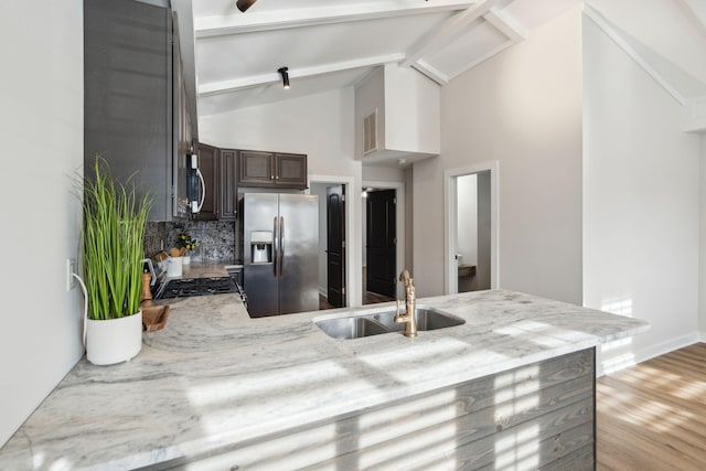 kitchen with sink, vaulted ceiling with beams, decorative backsplash, dark brown cabinets, and stainless steel appliances