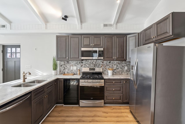 kitchen with appliances with stainless steel finishes, dark brown cabinetry, sink, beam ceiling, and light hardwood / wood-style floors