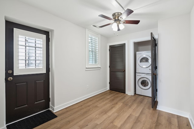 clothes washing area with stacked washer and dryer, light hardwood / wood-style flooring, and ceiling fan