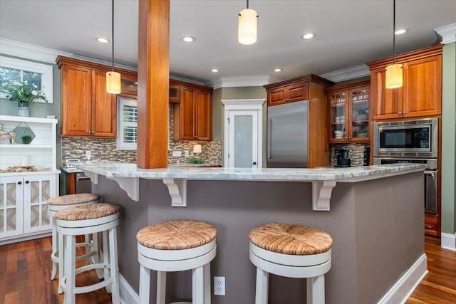 kitchen with a kitchen bar, built in appliances, hanging light fixtures, and light stone countertops