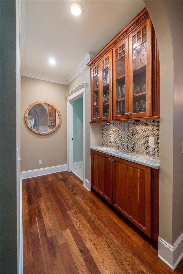 bar with backsplash, light stone counters, ornamental molding, and dark wood-type flooring