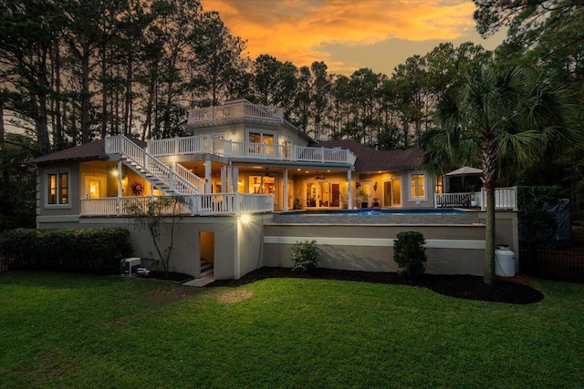 back house at dusk with ceiling fan, a balcony, and a yard